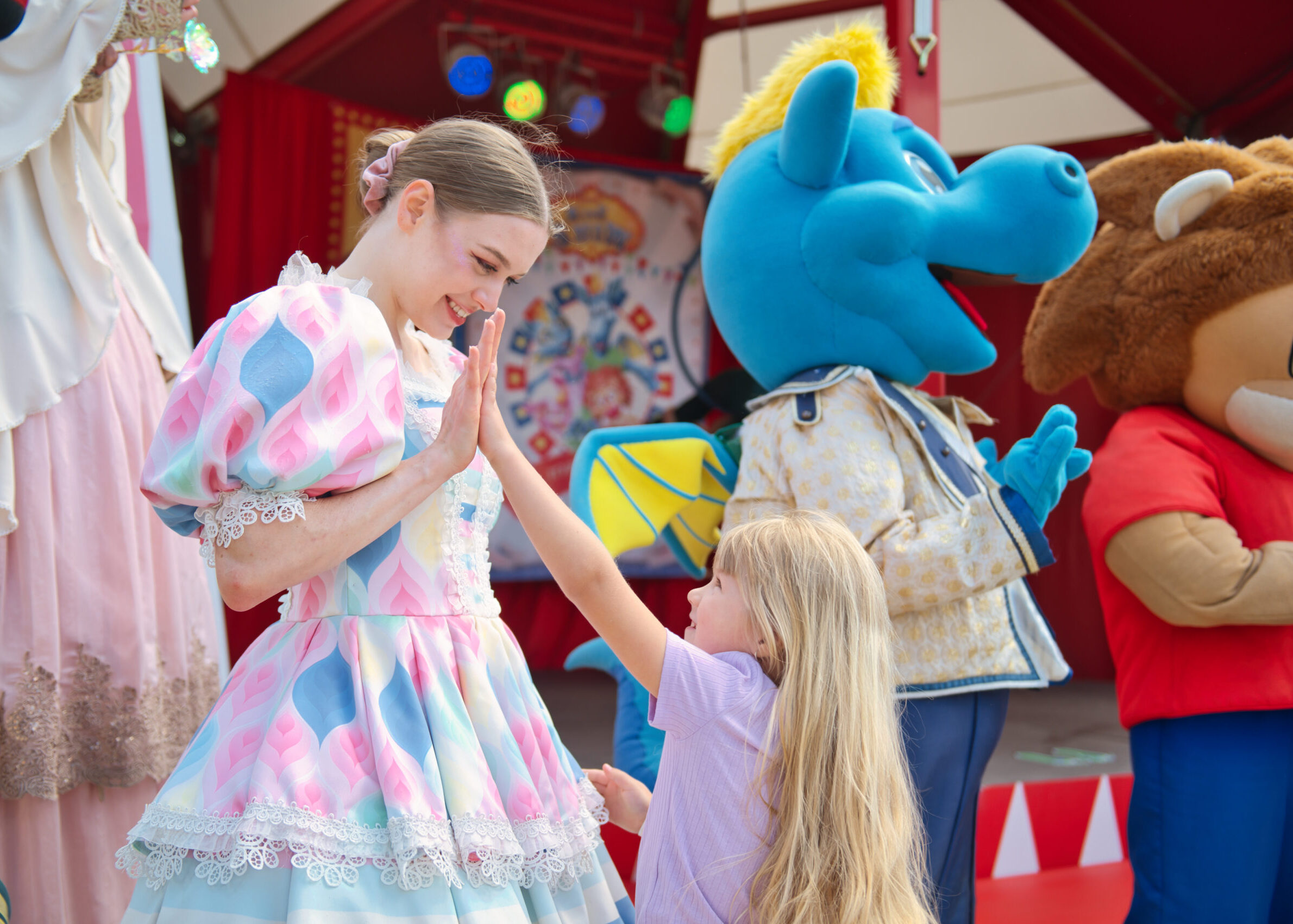 Dziewczynka przybijająca piątkę z aktorką w kolorowej sukni podczas występu w Energylandii, w tle maskotki i dekoracje sceniczne.