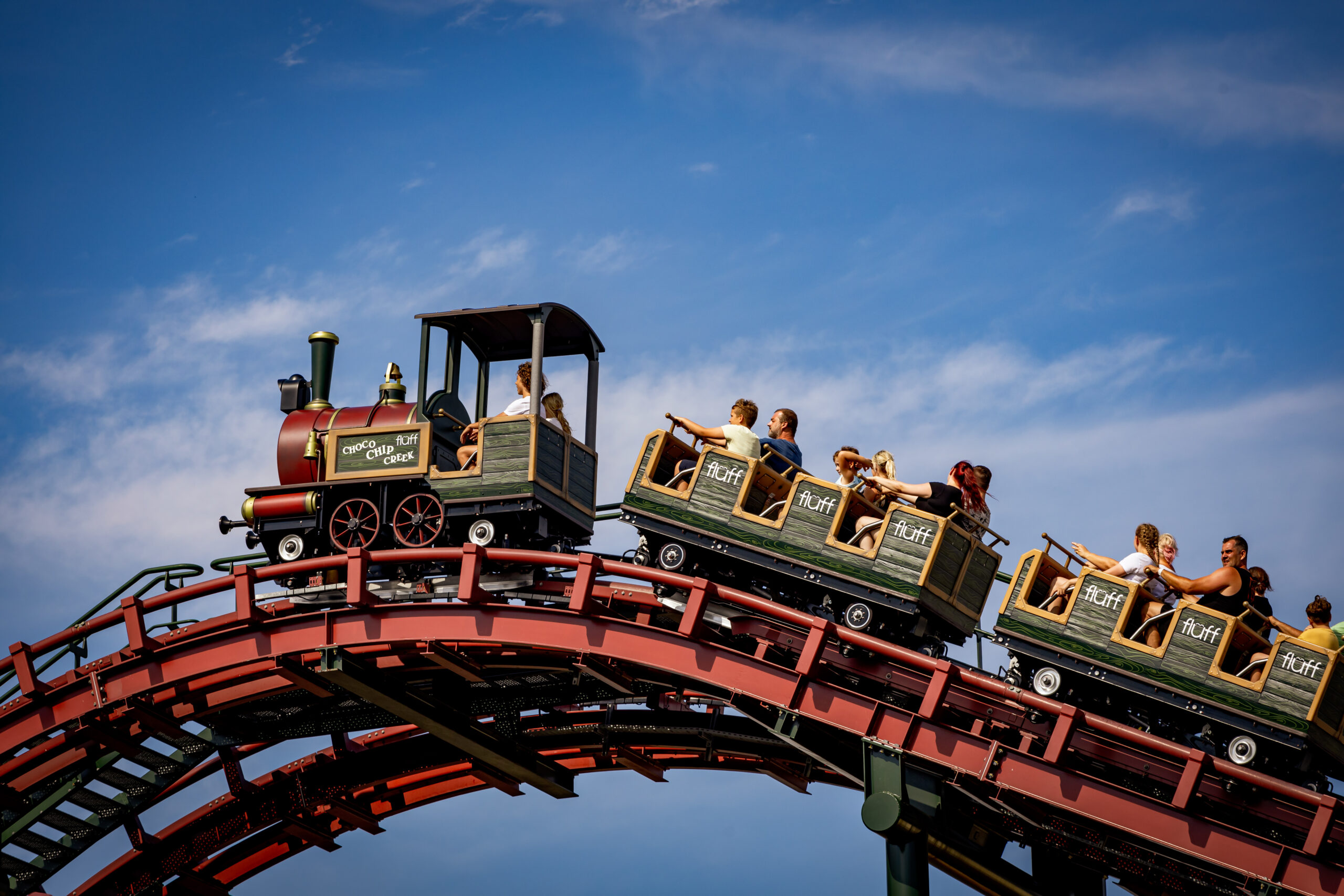 Rodziny i dzieci jadące kolejką w stylu pociągu „Fluff Choco Chip Creek” w Energylandii, na tle błękitnego nieba.